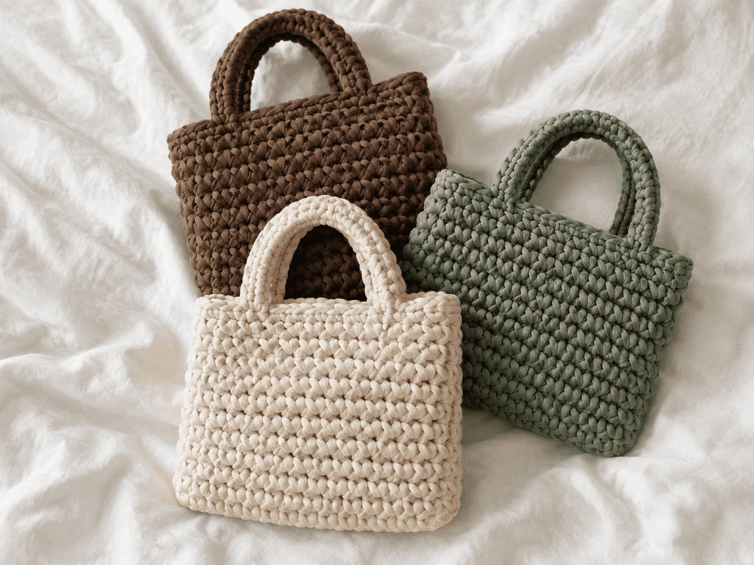 Three small chunky crochet handbags in brown, cream and sage green with arched built-in handles on a white sheet